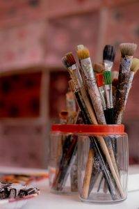Photo macro de deux pots qui contiennent des pinceaux de peintre de type brosse. Le corps des pinceaux est plein de peinture sèche.